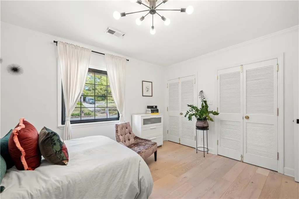 Bedroom featuring multiple closets, light wood-style flooring, ornamental molding, and a chandelier