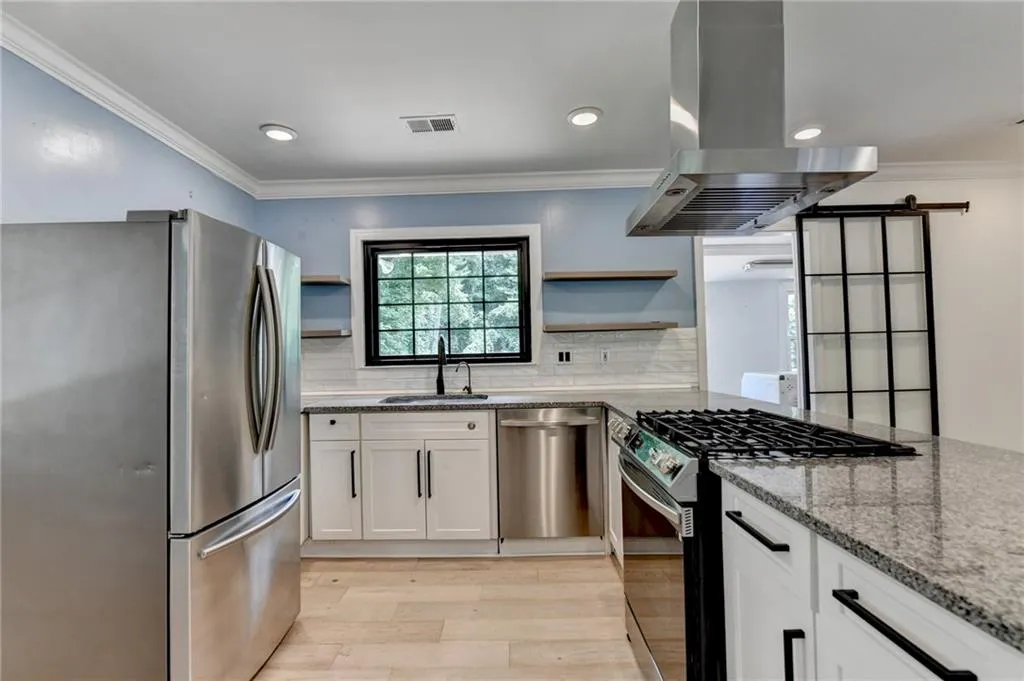 Kitchen featuring ornamental molding, appliances with stainless steel finishes, island exhaust hood, light stone counters, and light wood finished floors