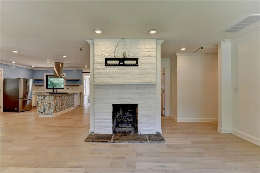 Unfurnished living room with ornamental molding, a stone fireplace, recessed lighting, and light wood-type flooring