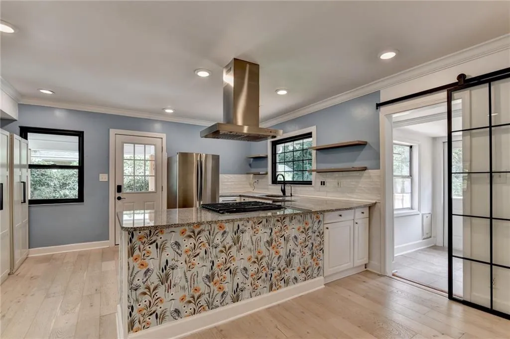 Kitchen with light stone counters, island exhaust hood, backsplash, freestanding refrigerator, and ornamental molding