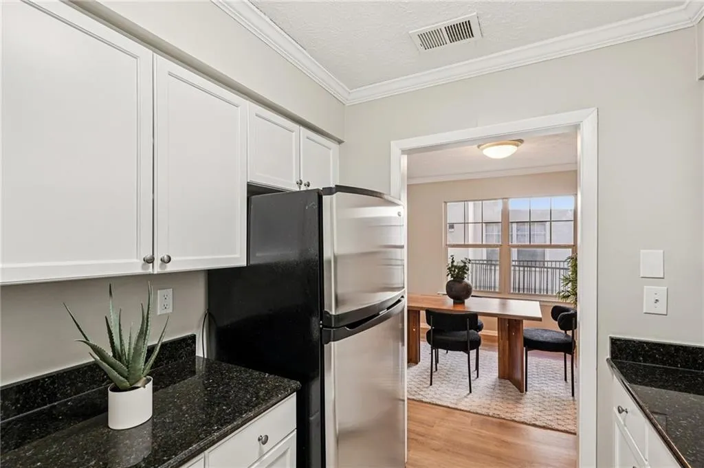 Kitchen featuring crown molding, white cabinets, light wood-style floors, dark stone countertops, and freestanding refrigerator