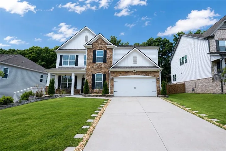 Two-story residence featuring a stone and siding facade, a two-car garage, and a covered front porch