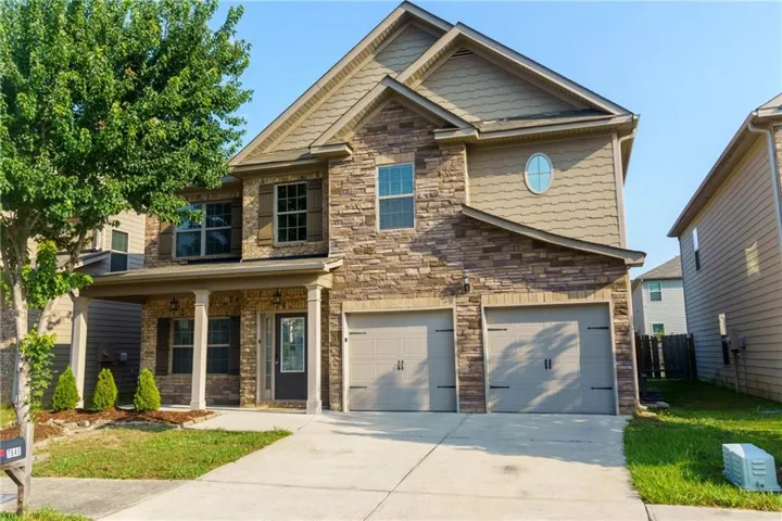 Two-story residence featuring a stone and siding facade, a double-bay garage with carriage-style doors, and a covered front porch with white columns
