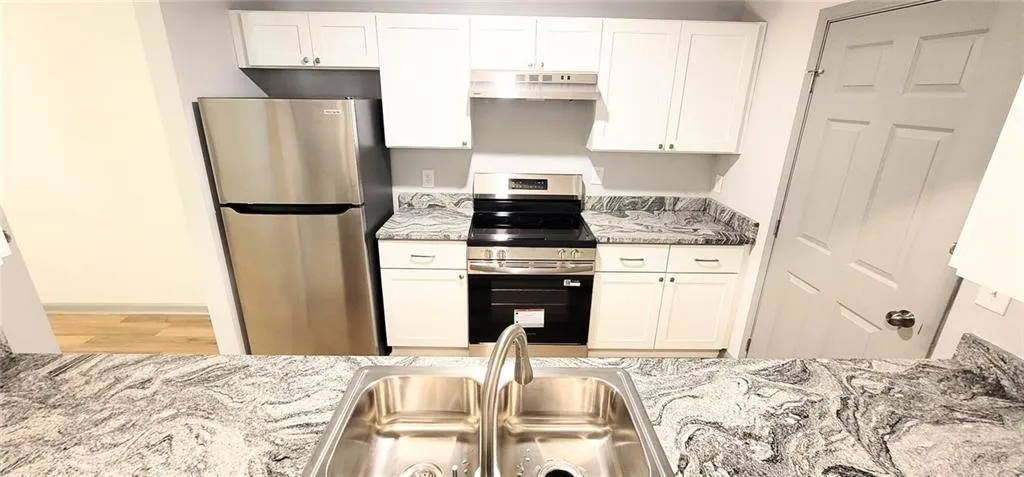 Kitchen featuring white cabinetry, stainless steel appliances, a stainless steel double basin sink, and beautiful stone countertops