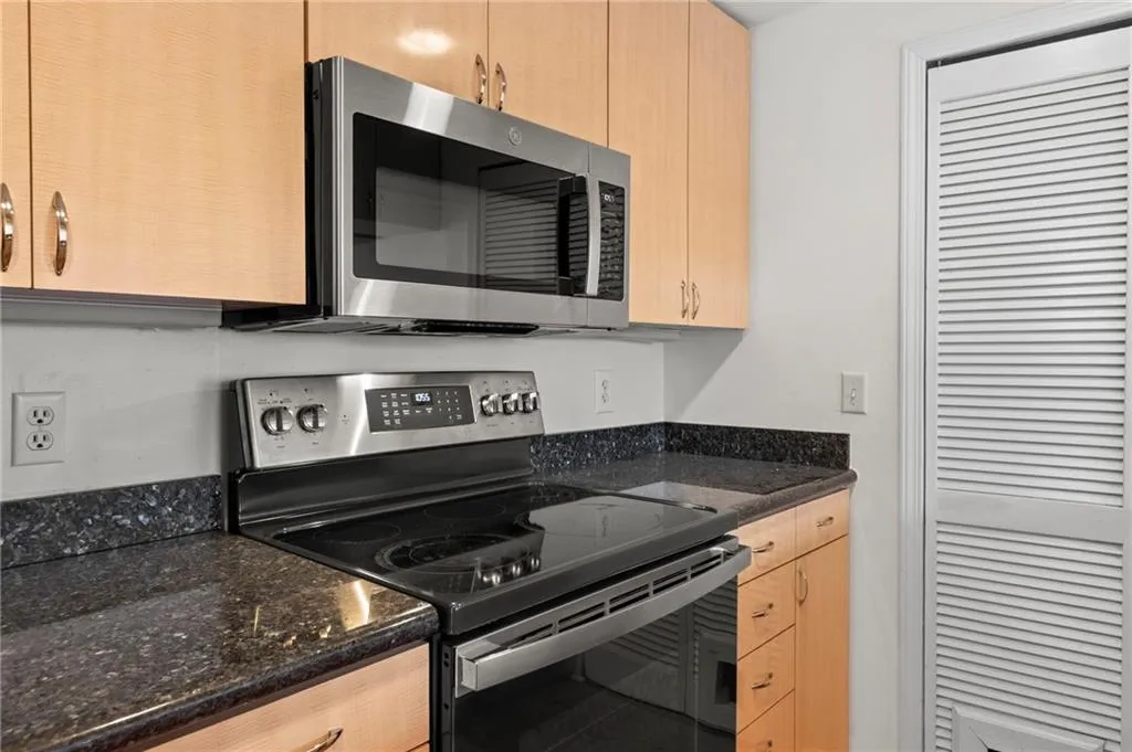 Kitchen featuring stainless steel appliances, dark stone counters, and light wood finish cabinetry