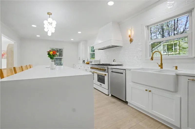 Kitchen with backsplash, high end stove, white cabinets, stainless steel dishwasher, and light stone countertops