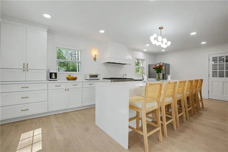 Kitchen with a center island with sink, white cabinetry, crown molding, light wood finished floors, and tasteful backsplash
