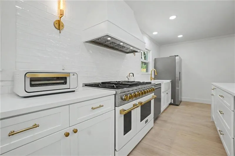 Kitchen with stainless steel appliances, ornamental molding, white cabinets, light wood-style flooring, and decorative backsplash