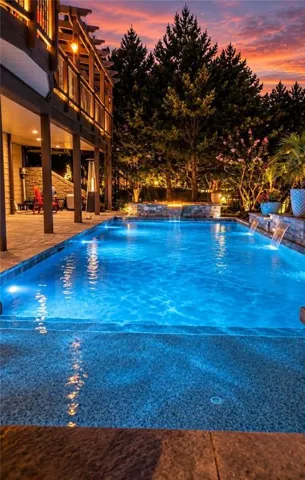 Illuminated swimming pool with integrated water features and a stone surround