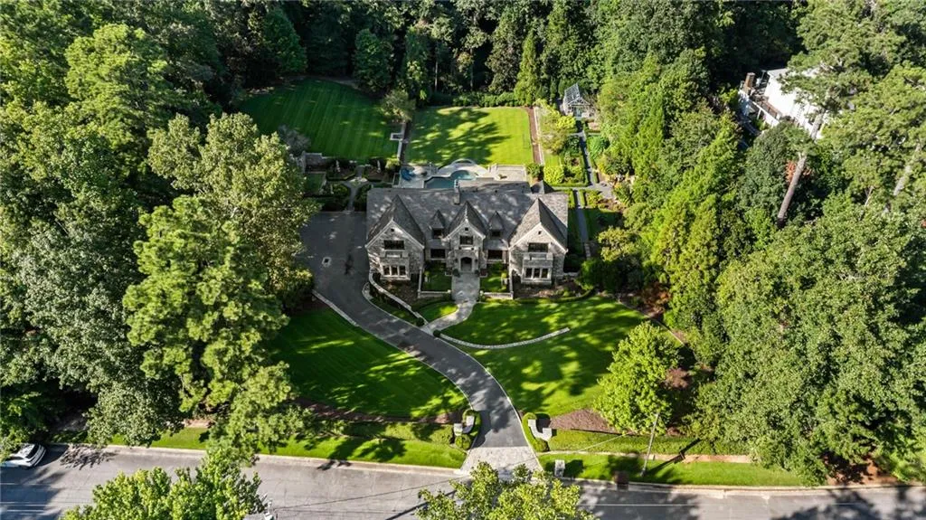 Stone-clad residence featuring a paved circular driveway, expansive manicured lawn, and mature trees