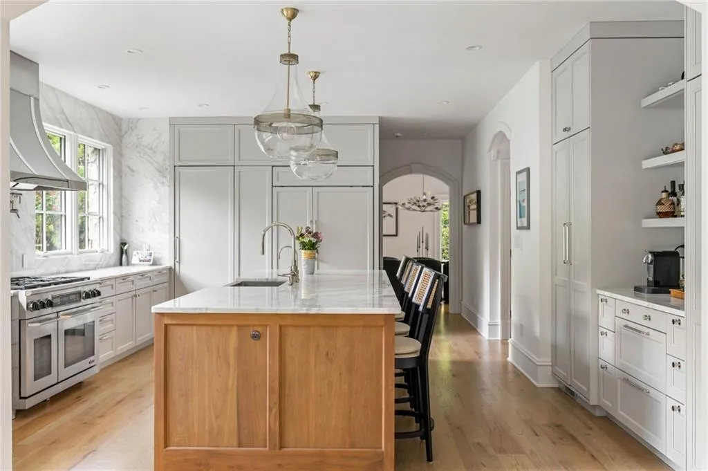 Custom cabinetry, stainless steel range with hood, wood-finish flooring, central island with seating, and integrated appliances