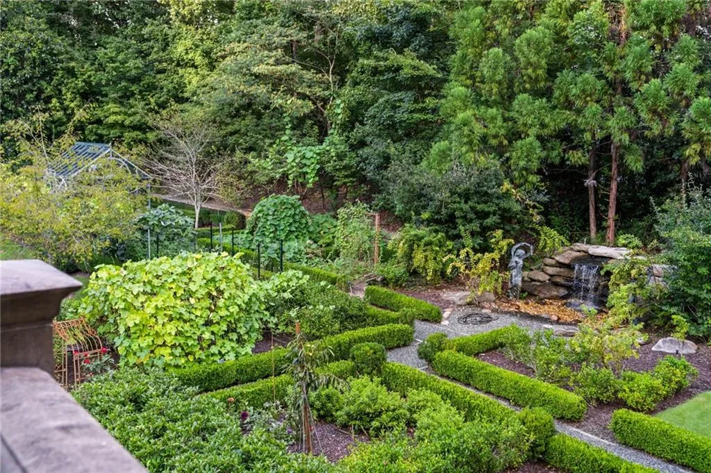 Expansive terraced garden featuring manicured hedges, a stone water feature with a waterfall, a greenhouse, and varied mature foliage