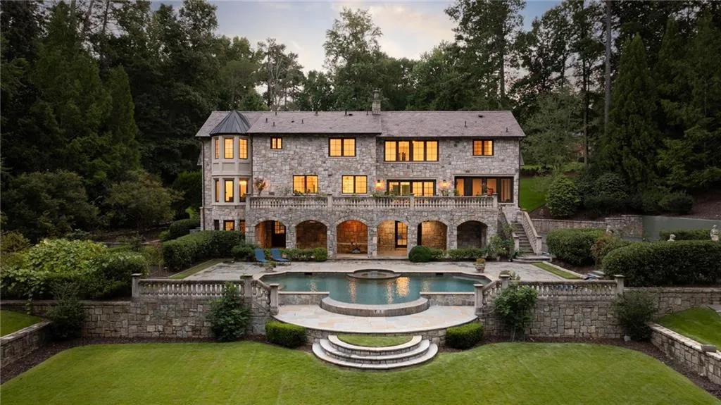 Stone exterior featuring multiple balconies, a lower-level arched patio, an outdoor pool with integrated spa, and tiered landscaping