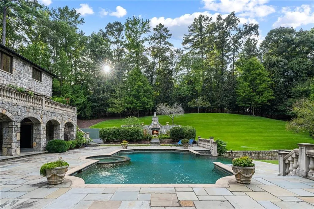 Stone facade construction with arched patio, stone balustrade, integrated swimming pool, attached hot tub, and expansive green lawn