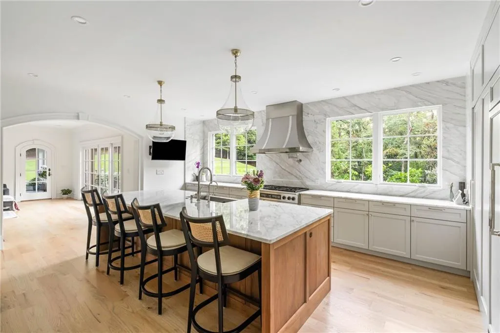 Kitchen featuring a large central island with seating, integrated appliances, marble backsplash, and wood-finish flooring
