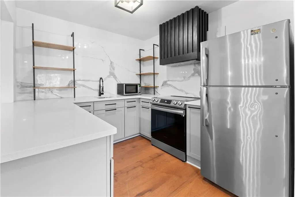 Kitchen with open shelves, stainless steel appliances, light wood-style flooring, and light stone counters