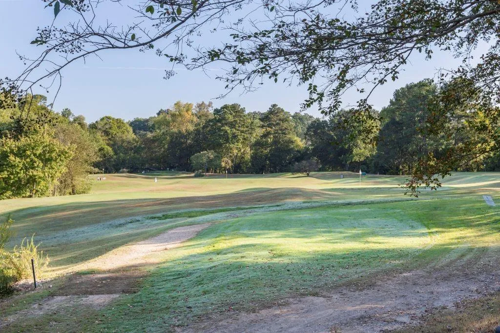 View of community with golf course view, a yard, and view of wooded area