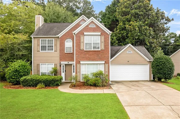 Two-story residence featuring a brick facade with complementary siding, an attached garage, a paved driveway, and a manicured lawn with established landscaping