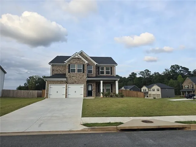 Brick facade home featuring a two-car garage, concrete driveway, and front lawn