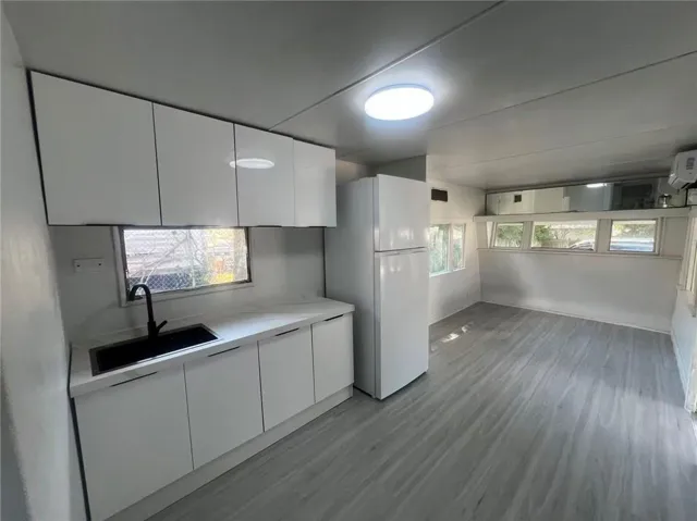 White cabinetry, black sink basin, black faucet, wood-finish flooring, and white refrigerator