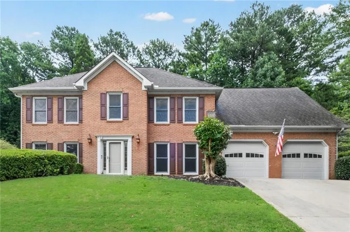 Brick exterior with gabled roofline, dual garage doors, decorative window shutters, and established perimeter landscaping