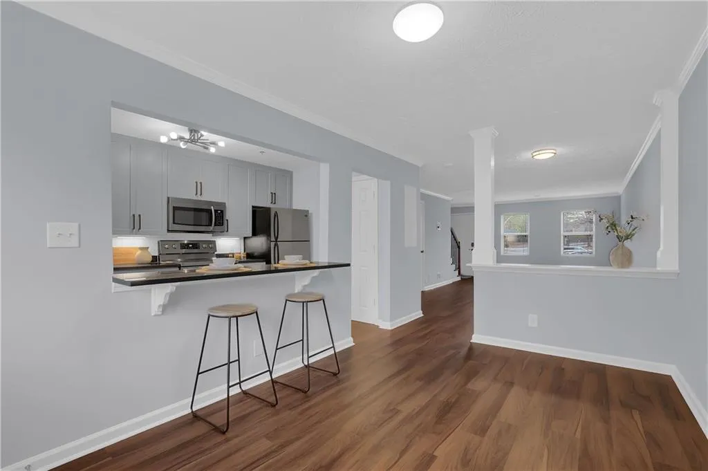 Kitchen featuring ornamental molding, a breakfast bar area, stainless steel appliances, dark wood-type flooring, and a notable chandelier
