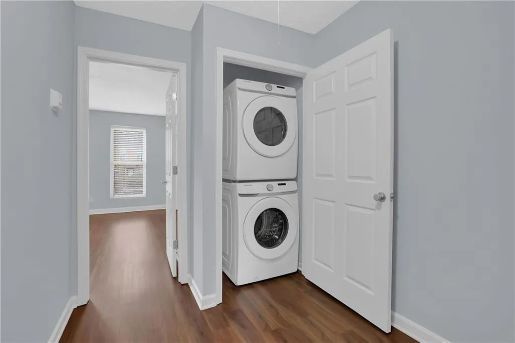Laundry area with stacked washer / drying machine and dark wood-type flooring