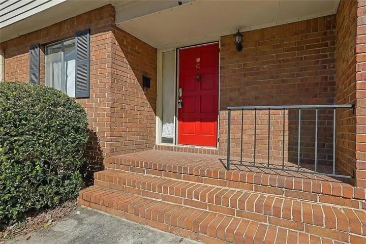 Brick exterior featuring a vibrant red entry door, brick steps, and a black metal railing