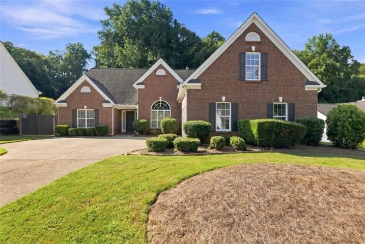 Brick exterior with white trim, arched window, dark shutters, and a concrete driveway
