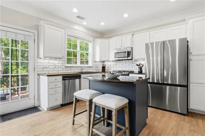Kitchen featuring white cabinetry, subway tile backsplash, stainless steel appliances, a center island with countertop seating, and wood-finish flooring