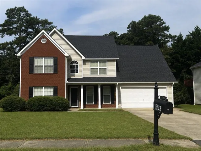 Brick and siding exterior with a two-car garage, manicured lawn, and mature trees