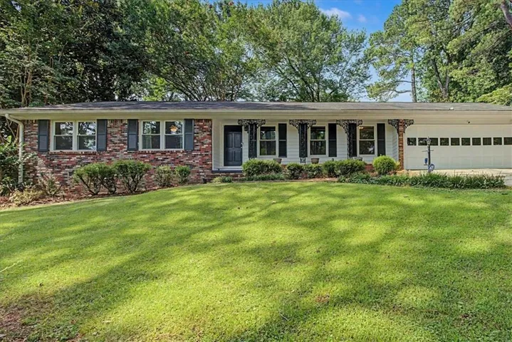 Brick and white siding exterior with a dark entry door, decorative porch columns, and a two-car garage