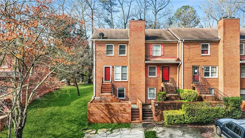 Brick townhome facade featuring dual-level entryways, red front doors, and red window shutters