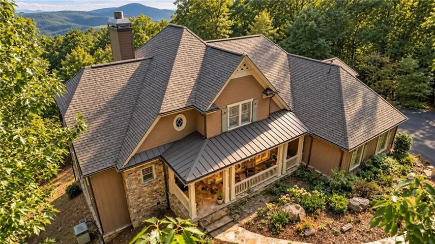 Craftsman-style residence featuring a stone and siding exterior, expansive covered porch, and a shingle roof with metal accents