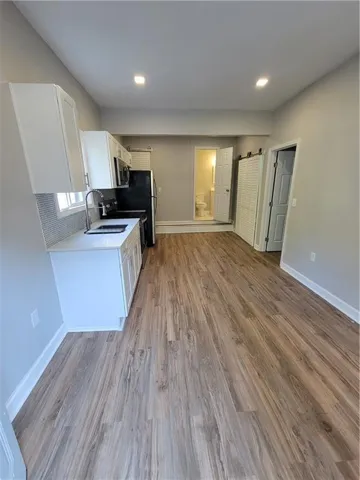 Kitchenette with white cabinetry, modern appliances, tile backsplash, and wood-finish flooring