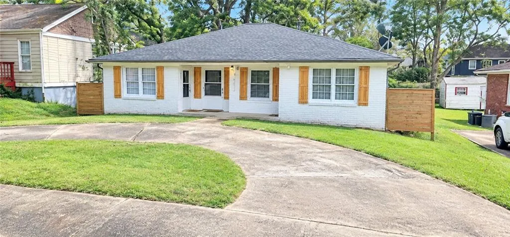 White brick exterior with a dark shingle roof, complemented by natural wood-tone shutters and a curved concrete driveway