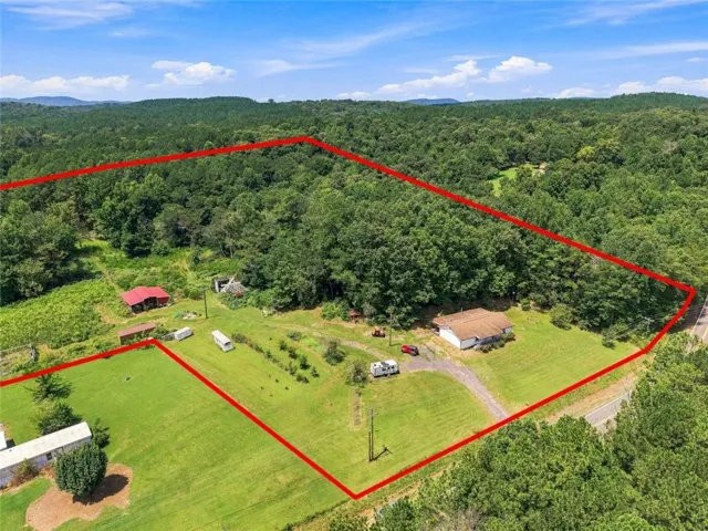 Expansive property featuring a single-story residence, secondary structure with a red roof, and established trees