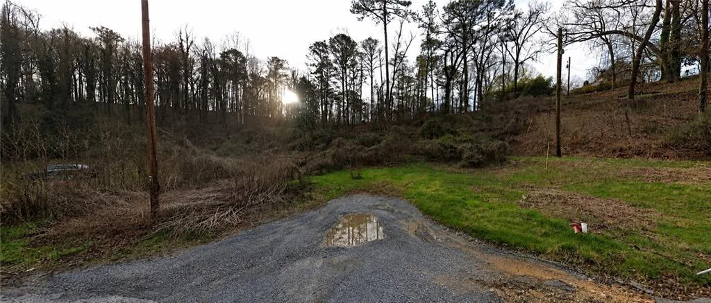 Gravel pathway opening onto a wooded lot with varying terrain and mature trees