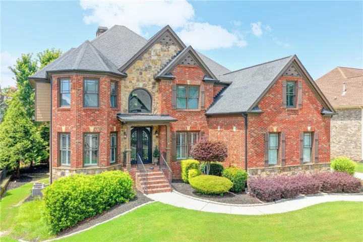 Brick exterior with stone accents, architectural shingle roof, arched transom window, and mature landscaping