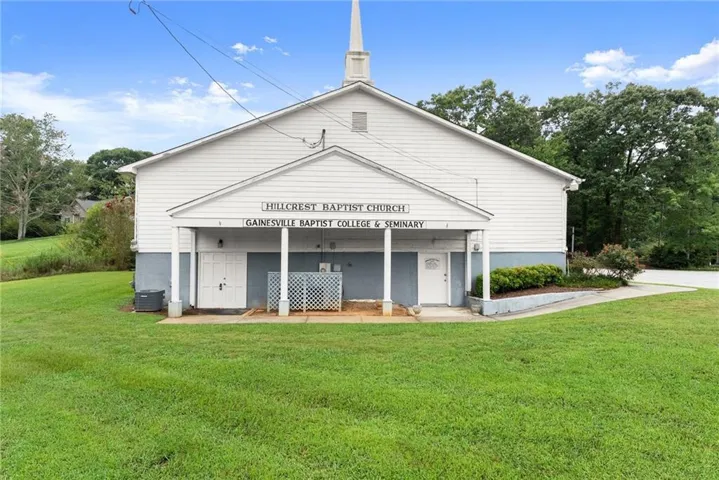 White siding exterior with a prominent steeple, covered entrance with columns, and a ramp leading to the entrance