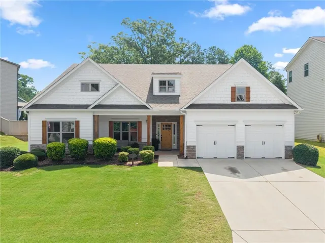 White multi-gabled exterior with shake and horizontal siding accents, stone detailing, a two-car garage, manicured shrubs, and a concrete driveway