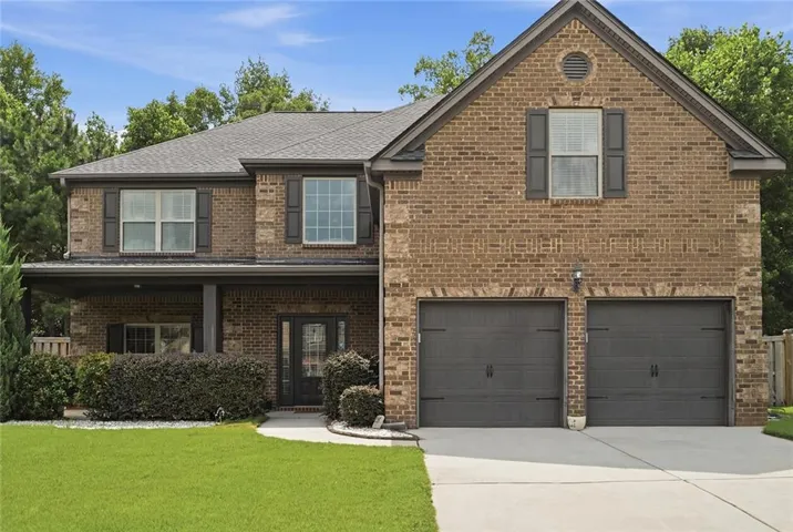 Two-story brick exterior featuring a covered front porch, a two-car garage with carriage-style doors, and a concrete driveway