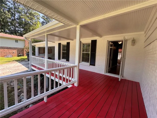 Covered front porch featuring a red wood-finish deck and white railing