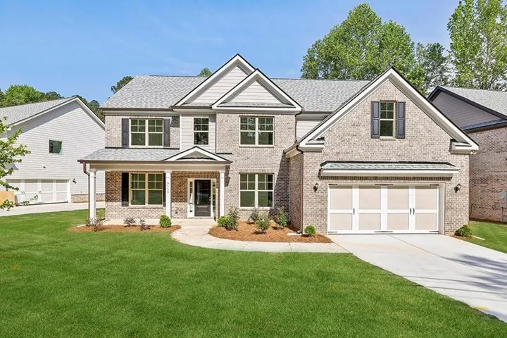 Two-story brick facade, gabled roofline, covered front porch, two-car garage with panel doors, and concrete driveway