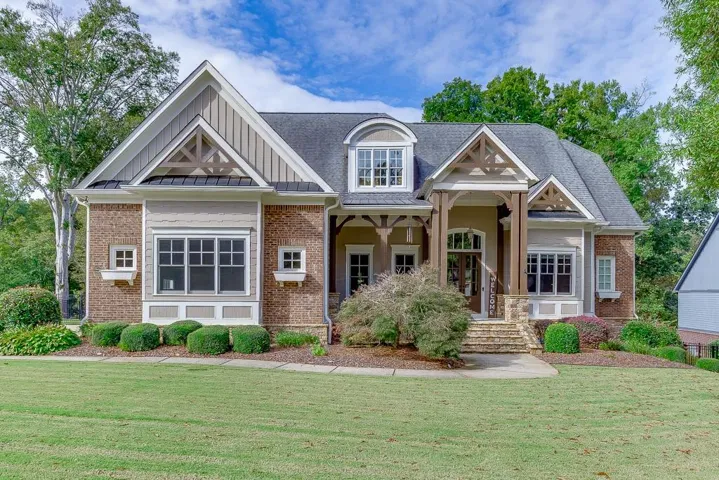 Craftsman-style exterior featuring a prominent gabled roofline, brick and siding facade, covered front porch with substantial columns, stone steps, and a dormer window