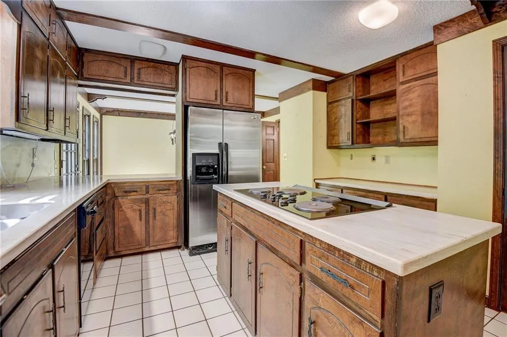 Kitchen featuring a textured ceiling, a center island, light tile flooring, and black appliances
