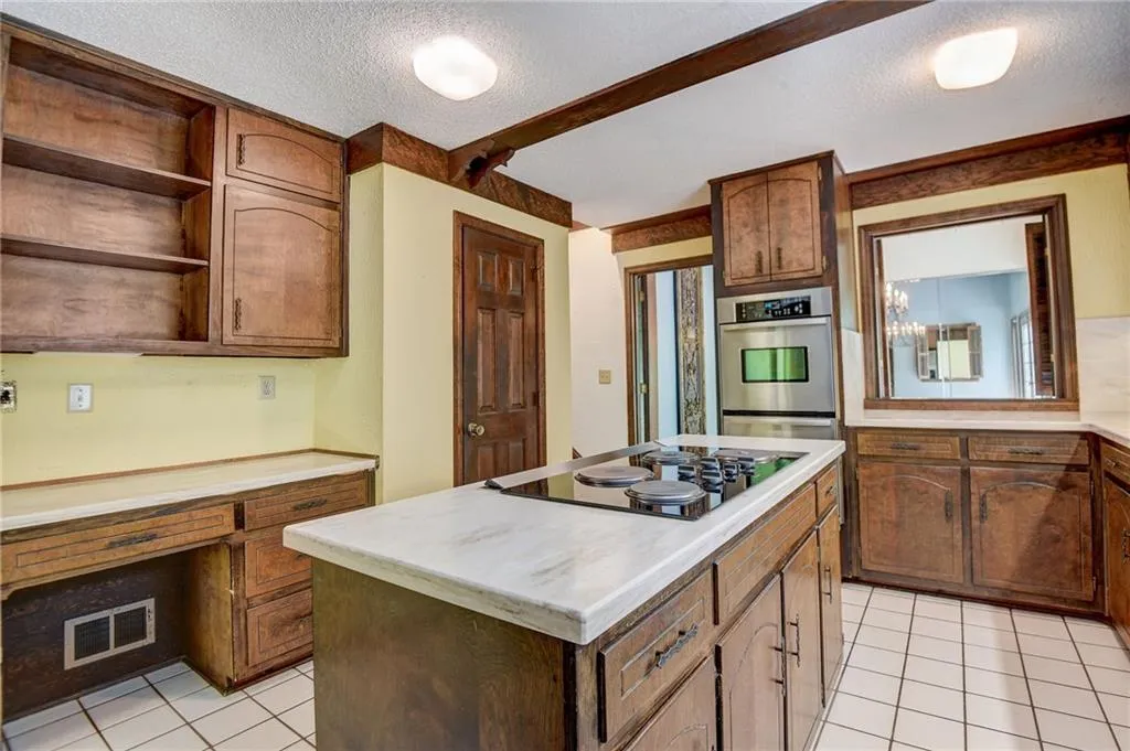 Kitchen with light tile flooring, a center island, black electric stovetop, and a textured ceiling
