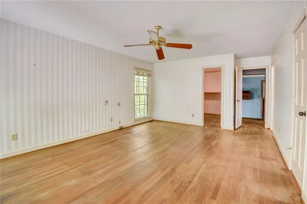 bedroom featuring a walk in closet, light hardwood / wood-style flooring, ceiling fan, and a textured ceiling