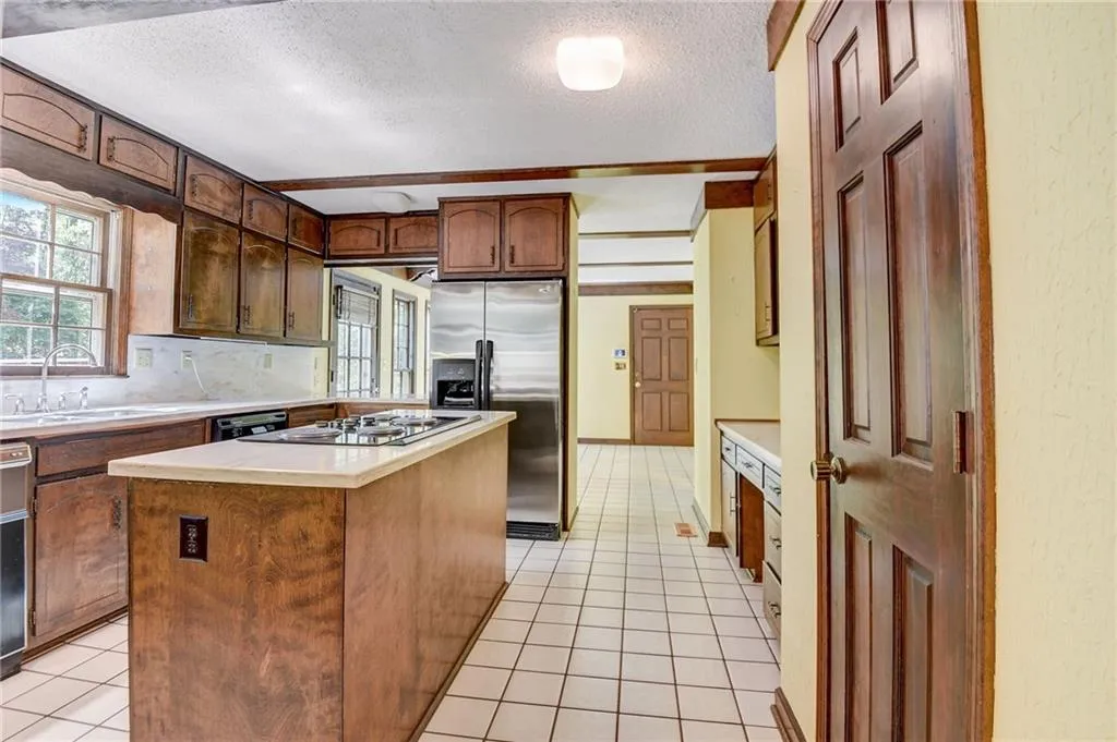Kitchen with light tile floors, a kitchen island, a textured ceiling, sink, and stainless steel refrigerator with ice dispenser
