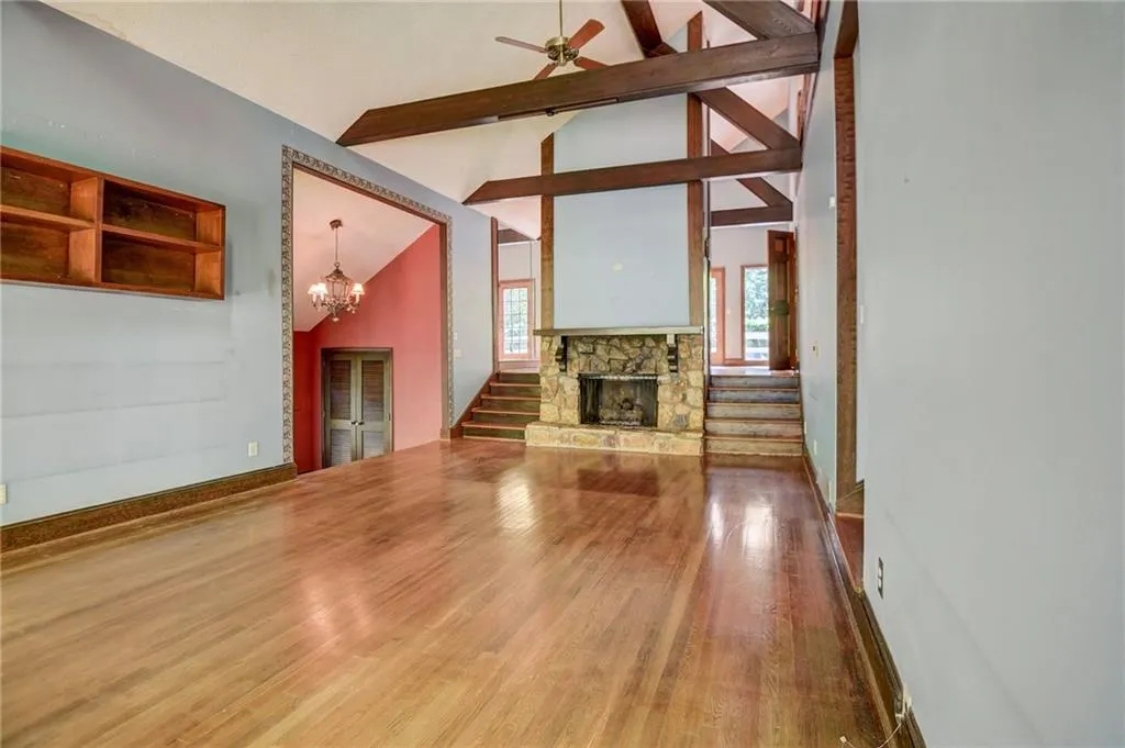 living room with beamed ceiling, a stone fireplace, high vaulted ceiling, ceiling fan with notable chandelier, and dark wood-type flooring